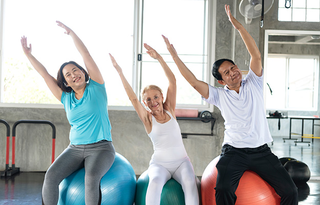 Group-friend-of-senior-at-yoga-gym-sitting-on-her-ball-smiling-and-happy-Bottom-Line---px-body